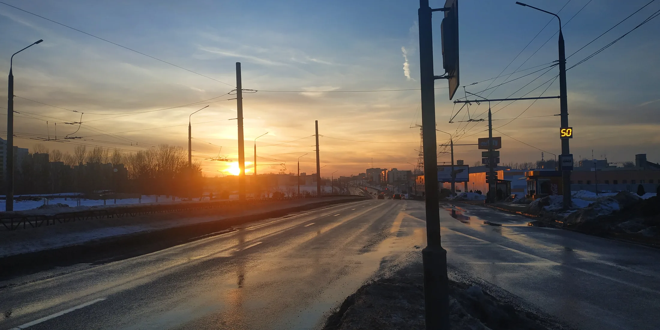 Рассвет на зимней дороге в Гродно, трамвайные провода, отражения на мокром асфальте
